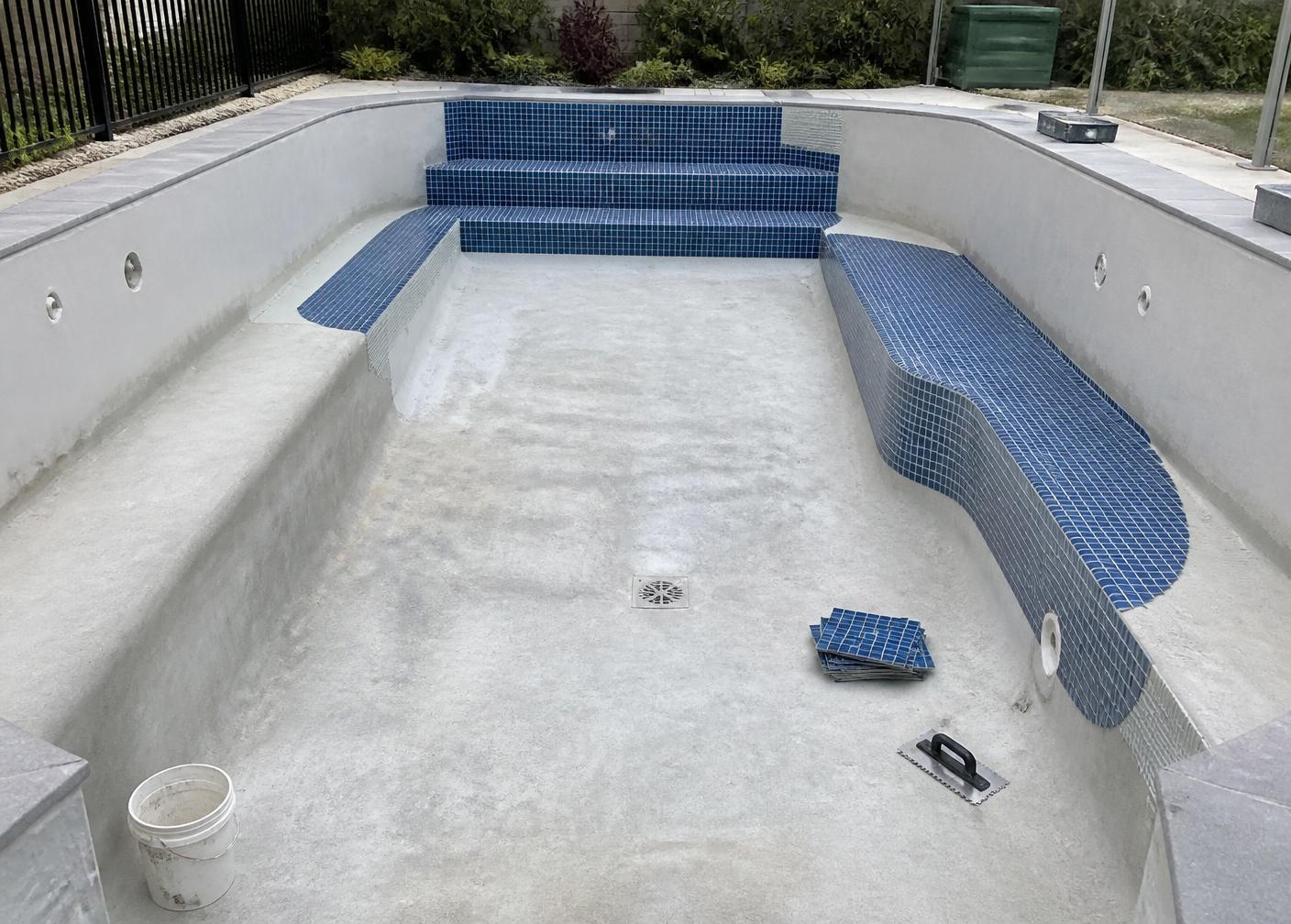 Pool shell being retiled with new blue mosaic on steps and bench seating