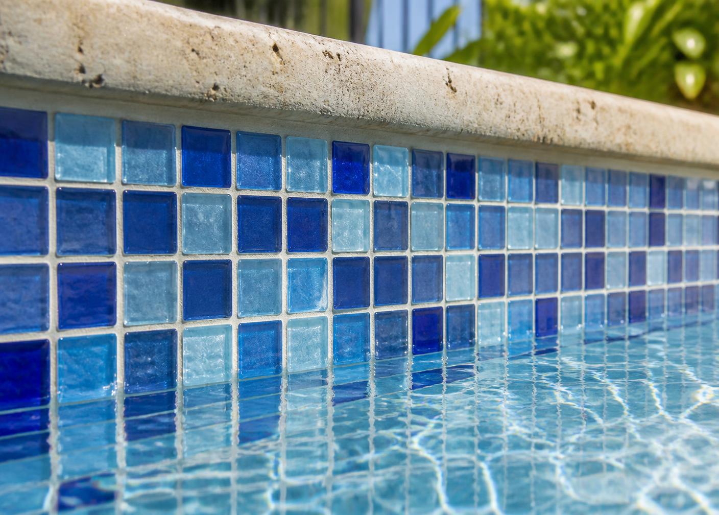 Close detail of graduated blue glass waterline mosaic beneath travertine pool coping